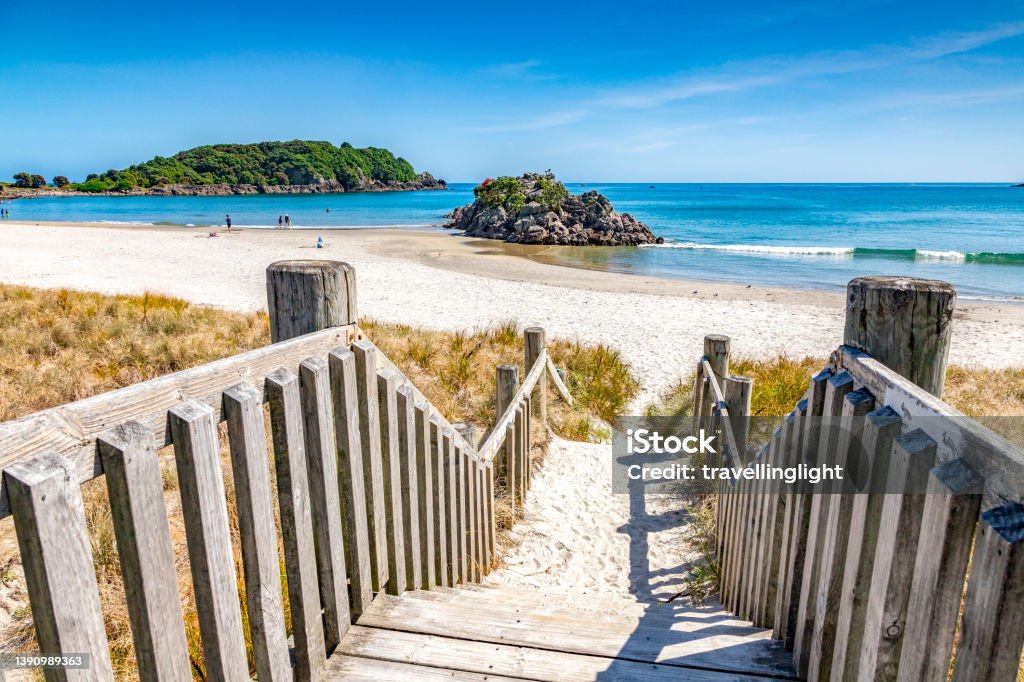 Steps to Beach, Mount Maunganui, New Zealand Mount Maunganui, Bay of Plenty, New Zealand - Steps down to beach on a beautiful summer day, with a small island and people walking at the edge of the sea. New Zealand Stock Photo