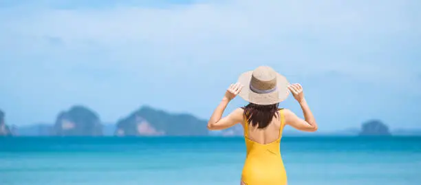Photo of Woman tourist in yellow swimsuit and hat, happy traveler sunbathing at Paradise beach on Islands. destination, wanderlust, Asia Travel, tropical summer, vacation and holiday concept