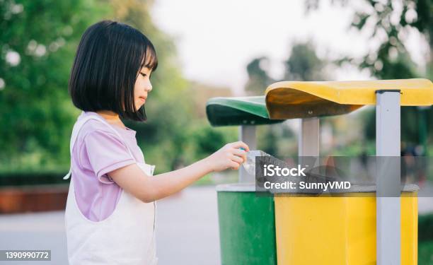 Image Of Asian Little Girl Puts Used Plastic Bottles In The Trash Stock Photo - Download Image Now