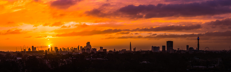 Golden light of dawn silhouetting the spires and skyscrapers of London, from the high-rises of Canary Wharf, past the towers of The City to the dome of St. Paul’s Cathedral, The Shard, Post Office Tower and Millennium Wheel.