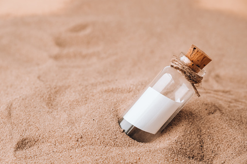 Letter in a bottle on the beach. Island lifestyle. Paper Message in a glass bottle with a cork on the sand. Note on salvation, please help. SOS concept. Copy space. Mockup blank