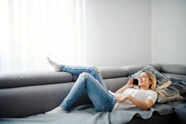 istock A happy woman enjoying the phone conversation while lying down on sofa. 1390992018