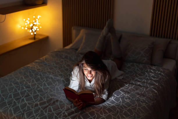 Woman reading a book in bed stock photo