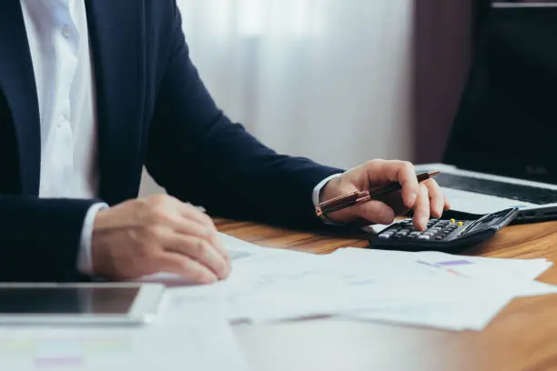 Photo of Close-up photo, businessman accountant's hand counts on a calculator, man sitting at a table paperwork