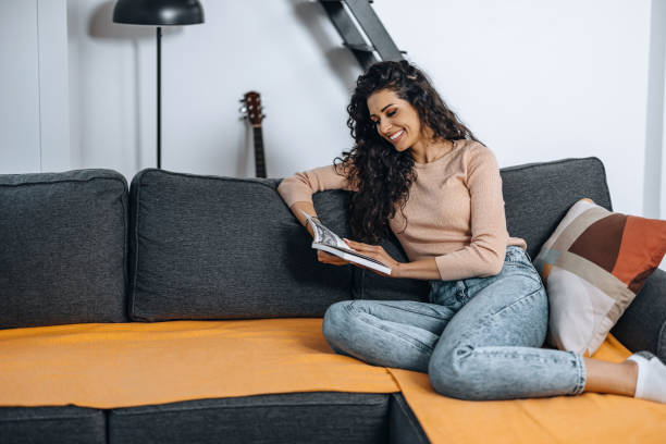 istock Young beautiful woman reading a book on the couch. 1390994935