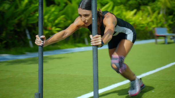 une jeune sportive brune européenne pousse un traîneau en acier pour le crossfit sur une pelouse verte - fitness trainer photos et images de collection