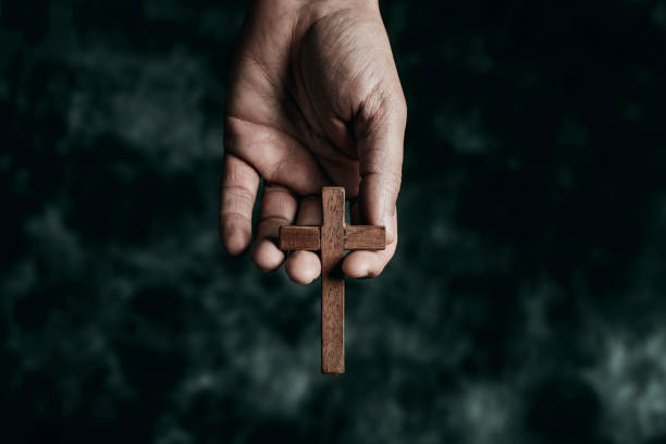 man holding a wooden cross in his hand a man is holding a wooden cross in his hand, on a black mottled background the passion of jesus stock pictures, royalty-free photos & images