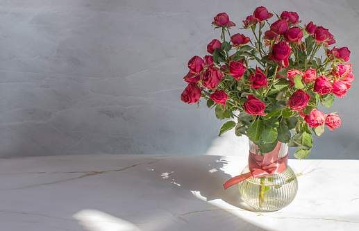 Bouquet of red roses in a glass vase, on a marble background. hard light