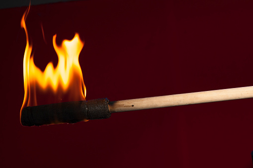 burning torch on a wooden base close-up on a burgundy background with empty space for text