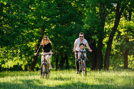 Mom, dad and their jolly son taking a bike ride through a countryside. Going past trees and fields.