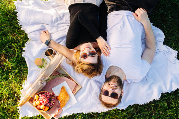 Happy couple resting on a blanket during picnic next to food box stock photo