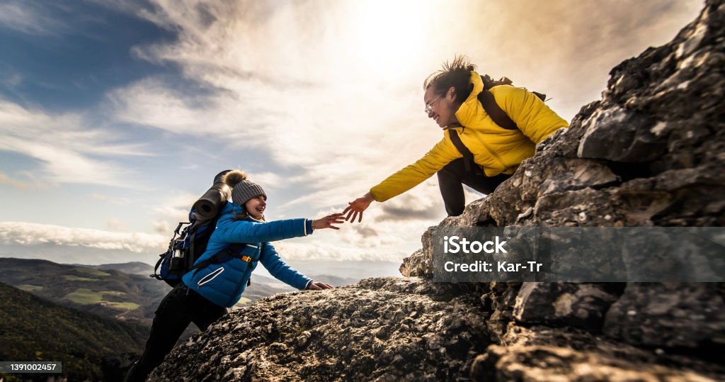 People helping each other hike up a mountain at sunrise - Giving helping hand and teamwork concept Support Stock Photo