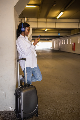 At the underground parking lot, young woman Black ethnicity , while using mobile phone, while waiting for transportation