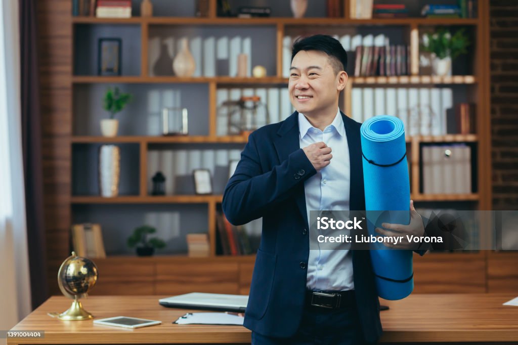 Businessman has finished his working day and is preparing for fitness, Asian is working in a classic office, late, man is holding a mat for fitness Exercising Stock Photo