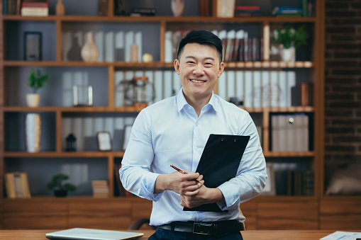 Retrato de un exitoso profesor asiático, un hombre con camisa mirando a la cámara y sonriendo, en la clásica oficina del director de la universidad photo