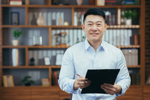 retrato de um financista de sucesso, asiático de camisa olha para a câmera e sorri em um escritório clássico - musical staff - fotografias e filmes do acervo