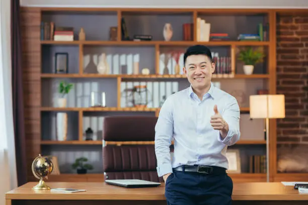 Photo of Portrait of a successful university principal, Asian teacher in a shirt looks at the camera and smiles, keeps his finger up, encourages young people to study at the university