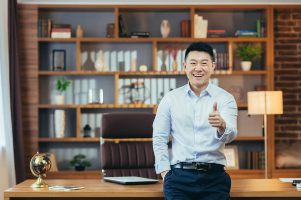 istock asian boss holding thumbs up on hands looking at camera and smiling, man working in office, portrait of successful and affirmative businessman 1391004435