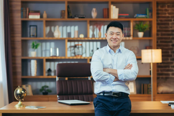 クラシックなオフィスで働く成功したビジネスマンの肖像画、腕を組んでカメラを見つめるアジア人の笑顔と幸せ - 最高経営責任者 ストックフォトと画像