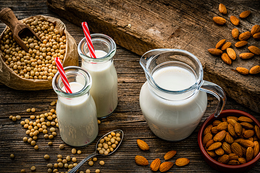 High angle view of a glass bottle and a jar filled with soy milk and almond milk shot on rustic wooden table. Soy beans are around the bottles. High resolution 42Mp studio digital capture taken with Sony A7rII and Sony FE 90mm f2.8 macro G OSS lens