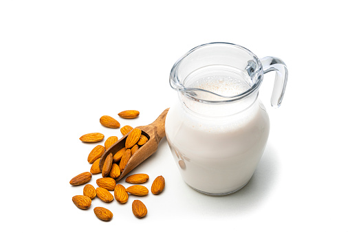 High angle view of a glass jar filled with almond milk isolated on white background. Peeled almonds are around the jar. The composition is at the right of an horizontal frame leaving useful copy space for text and/or logo at the left. High resolution 42Mp studio digital capture taken with Sony A7rII and Sony FE 90mm f2.8 macro G OSS lens
