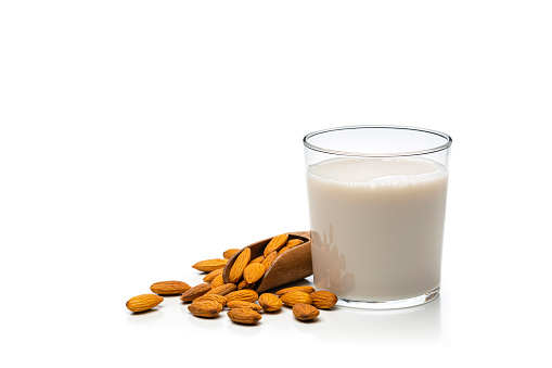 Front view of a glass filled with almond milk isolated on white background. Peeled almonds are around the glass. The composition is at the right of an horizontal frame leaving useful copy space for text and/or logo at the left. High resolution 42Mp studio digital capture taken with Sony A7rII and Sony FE 90mm f2.8 macro G OSS lens