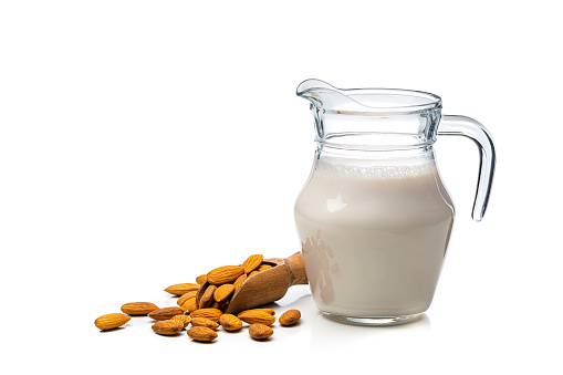 Front view of a glass jar filled with almond milk. Peeled almonds are around the jar. The composition is at the right of an horizontal frame leaving useful copy space for text and/or logo at the left. High resolution 42Mp studio digital capture taken with Sony A7rII and Sony FE 90mm f2.8 macro G OSS lens