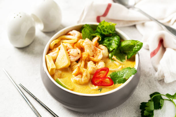 istock Asian laksa soup with shrimp in a ceramic bowl on a light culinary background. Spicy broth soup with coconut milk, rice noodles and seafood in a plate on the closeup kitchen table closeup 1391015458