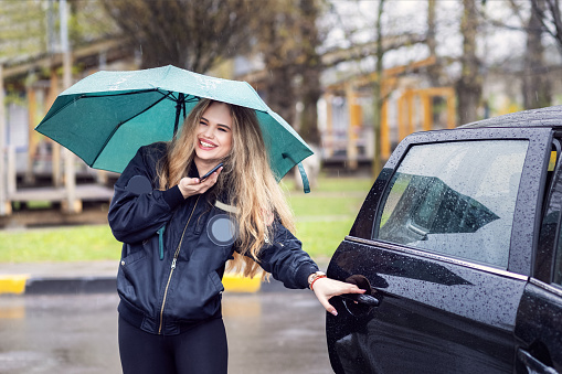 Happy young woman with umbrella getting in taxi car in rainy day