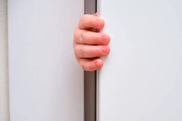 Toddler baby boy holds the edge of the open door with his hand. Close-up child hand at the door jamb