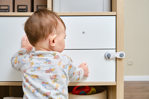 Toddler baby boy rips off a cabinet drawer with his hand. The child holds the cabinet door handle, small kid