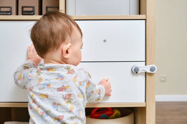 маленький мальчик срывает ящик шкафа рукой. ребенок держит дверную ручку шкафа, маленький ребенок - child proof стоковые фото и изображения
