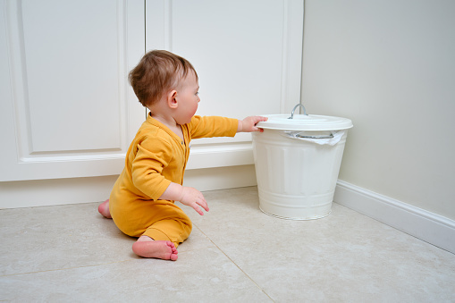 Toddler baby boy opens a trash can with household waste. Children's safety issues in the home room, little kid