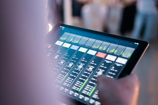 Close up shot of unrecognizable male hands using iPad for mixing music levels.