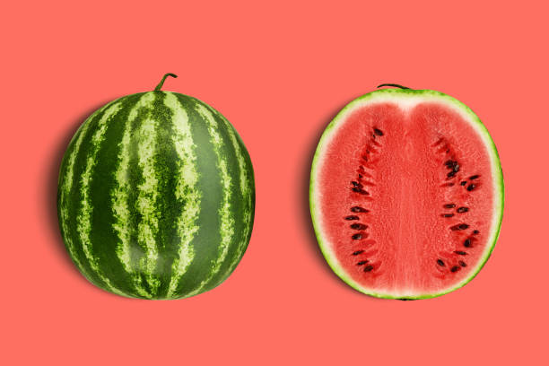 Green, striped watermelon, pink background with copy space for text, images. Cross-section. Berry with red flesh, black seeds. Top view. Close-up stock photo