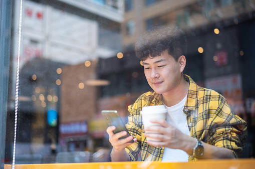 Asian handsome young man using smartphone in coffee shop