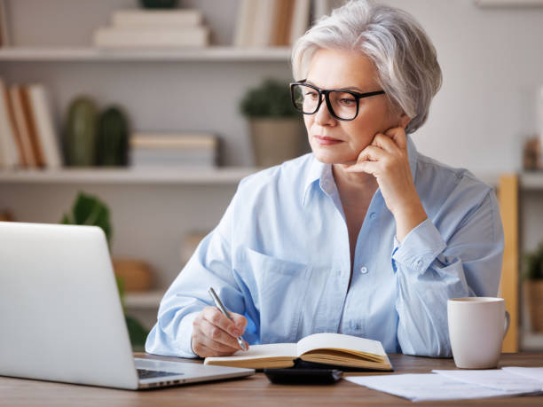 istock Mature businesswoman working at laptop, reading documents and take notes in home office 1391032614