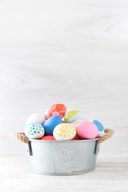 Easter eggs painted in pastel colors in a basket on white wooden background.