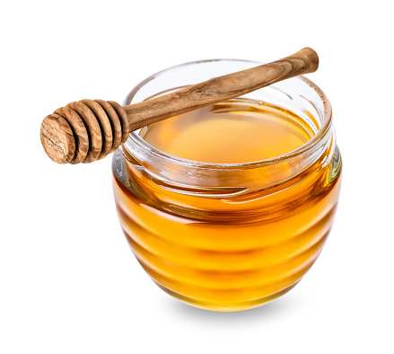 Glass jar with honey and wooden honey dipper with honey drop isolated on white background.