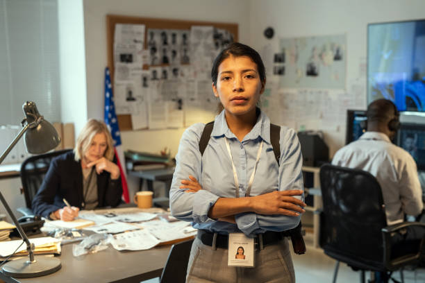 Young Hispanic female leader of intelligence service or police department Young Hispanic female leader of intelligence service or police department in uniform crossing arms on chest while standing against coworkers chief leader stock pictures, royalty-free photos & images
