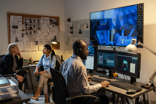 Agente afroamericano del FBI sentado frente a los monitores de la computadora y la pantalla photo
