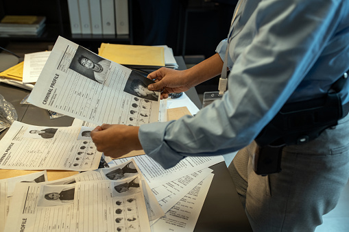 Young contemporary investigator holding criminal profile of gang leader over workplace while learning his personal information