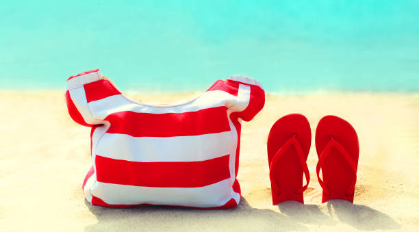 Summer vacation concept - red bag with flip flops on beach over blue sea background