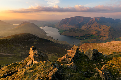 Breathtaking views of Crummock Water and Grasmoor Fells from Red Pike in the English Lake District. Golden side light can be seen illuminating some rocks in the foreground with a beautiful sky out towards the Cumbrian Coast.