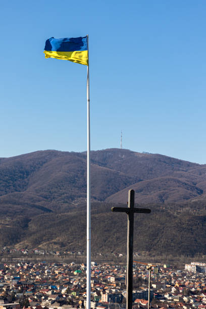 Ukrainian flag and cross on the background of mountains. Ukrainian flag and cross on the background of the landscape of the town in the mountains. ukrainian village stock pictures, royalty-free photos & images
