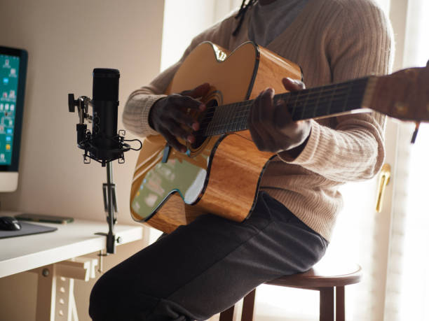 il giovane sta cantando e suonando la chitarra mentre fa una registrazione audio a casa - folk music audio foto e immagini stock