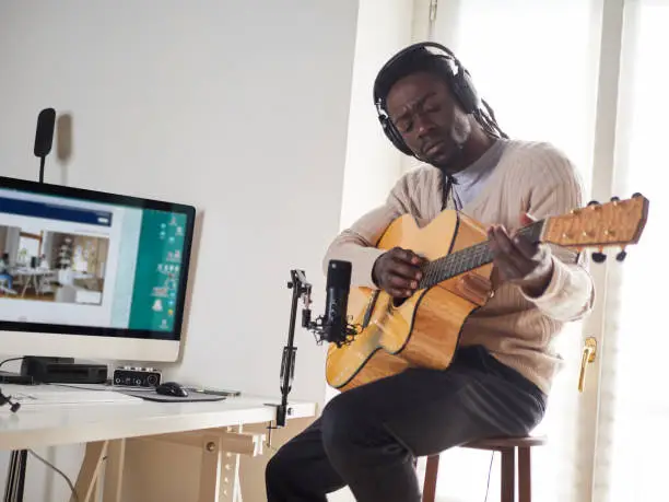Photo of Young man is singing and playing guitar while making an audio recording at home