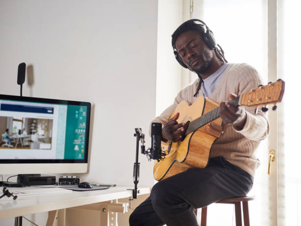 il giovane sta cantando e suonando la chitarra mentre fa una registrazione audio a casa - folk music audio foto e immagini stock