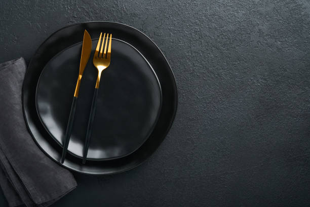 istock Ceramic empty black plate, silverware and linen kitchen towel napkin on old black ceramic cement concrete table background. Cooking stone backdrop. Top view with copy space. Flat lay 1391057109