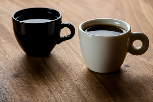 Two black and white full coffee cups on wooden background